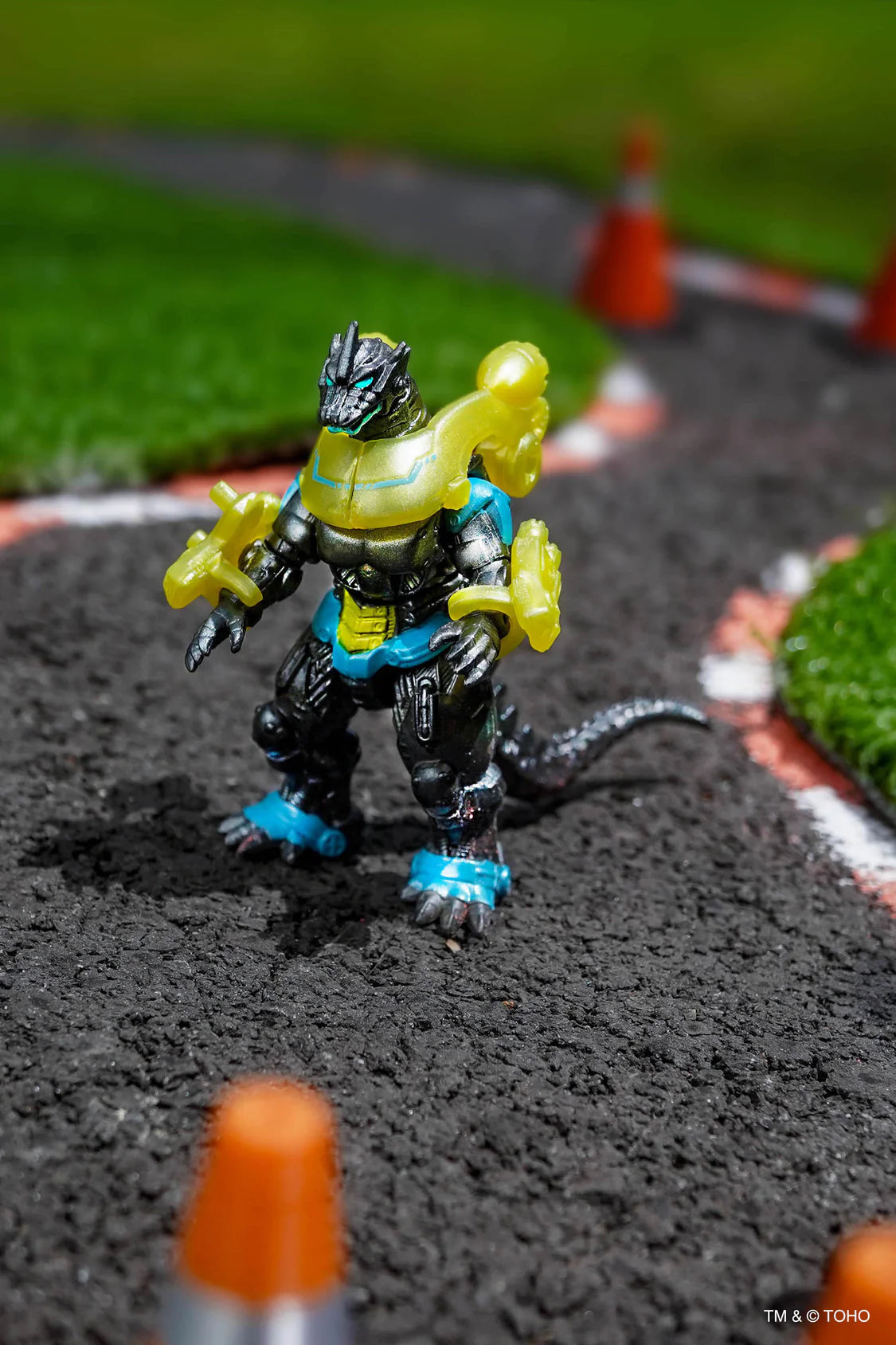 A small toy action figure of Type 3 Mechagodzilla, standing on a miniature racetrack with artificial grass, orange cones, and blurred background elements. - Action Figures - Movies - Godzilla & Kong