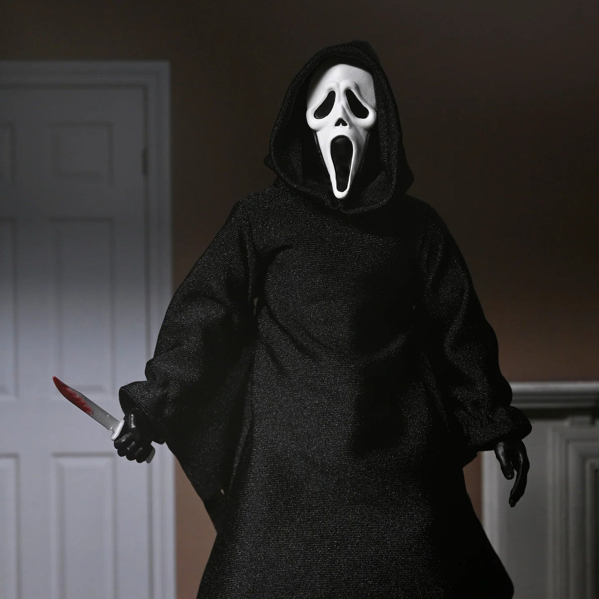 Person wearing a black hooded costume with a white mask holding a knife in a dimly lit room. - Action Figures - Horror
