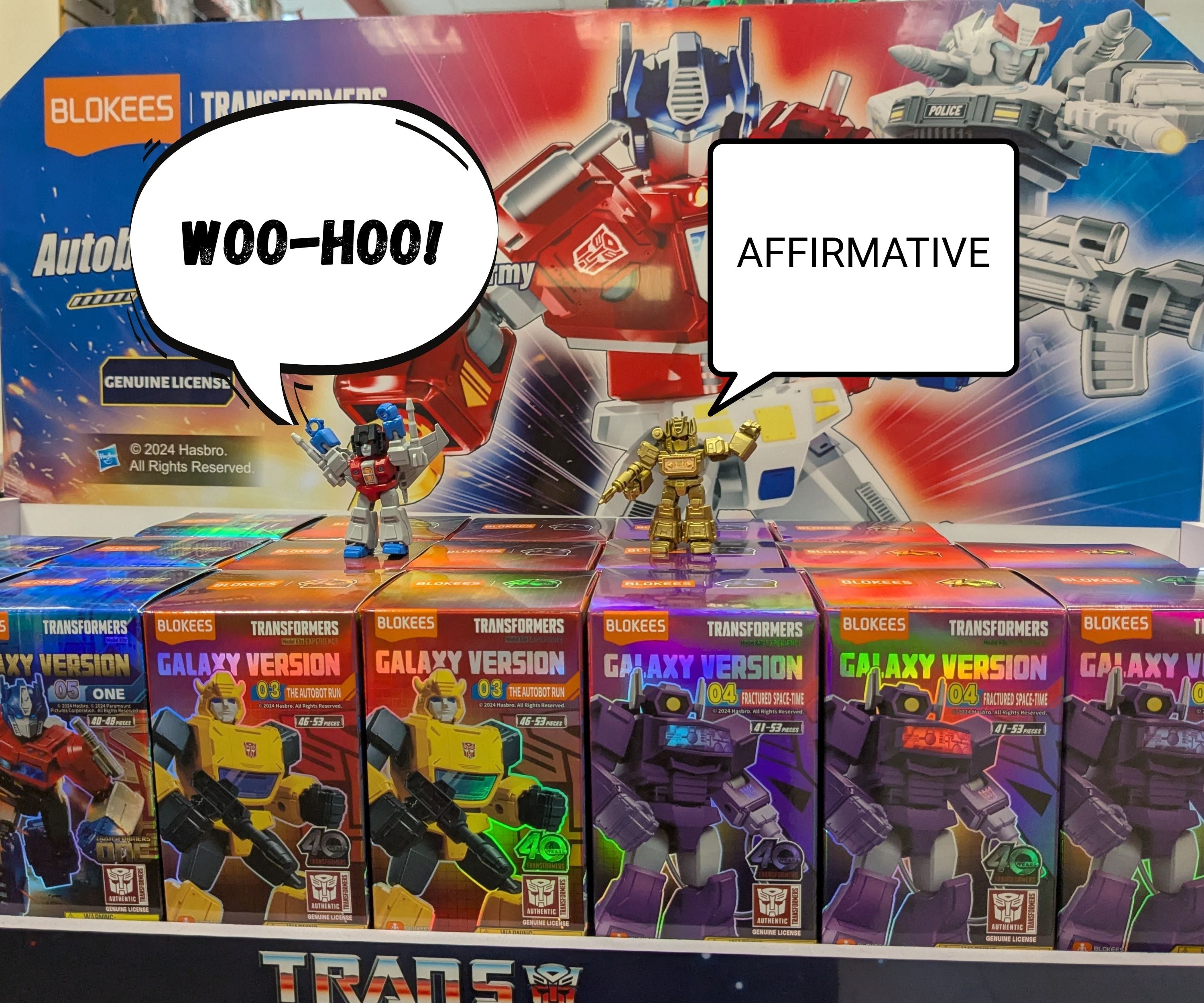 Transformers toy figures and boxes with speech bubbles and branding in the background