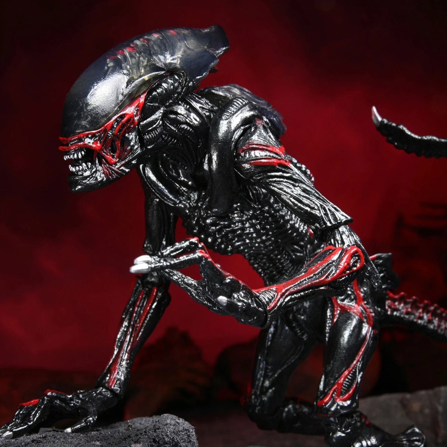 Alien action figure on a dark surface with a red background