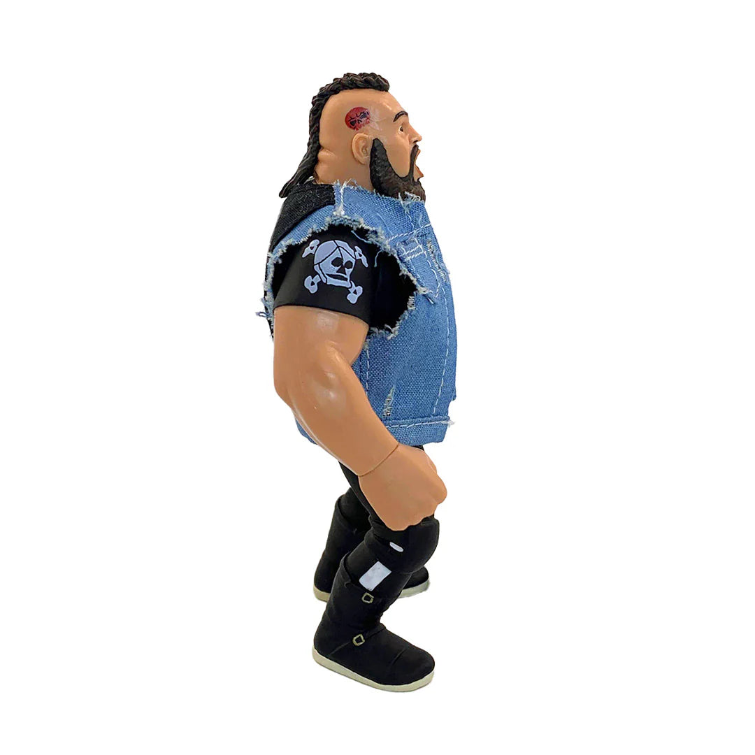 A wrestling action figure shown in side profile against a plain white background. The figure has dark hair, a beard, a blue distressed denim vest, a black shirt with a white skull-and-crossbones patch, black boots, and black shin wraps. - Action Figures - Wrestling