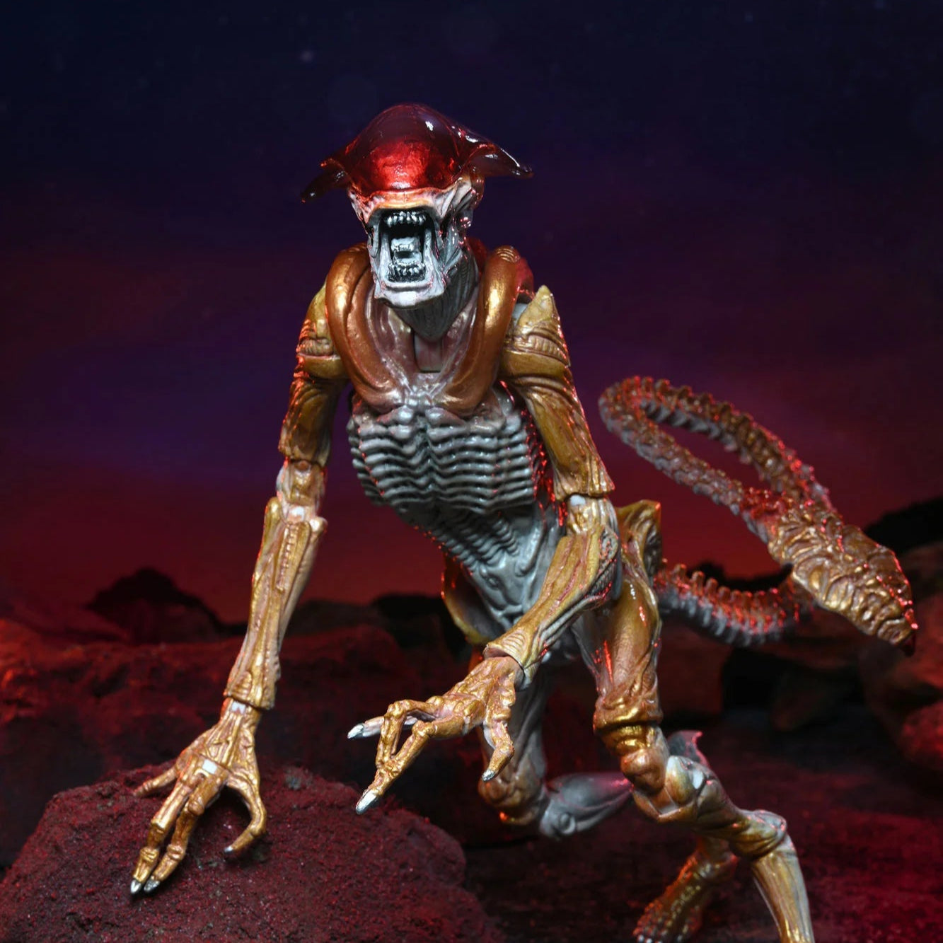 Alien-like creature figure on a dark, rocky surface with a red light on its head.