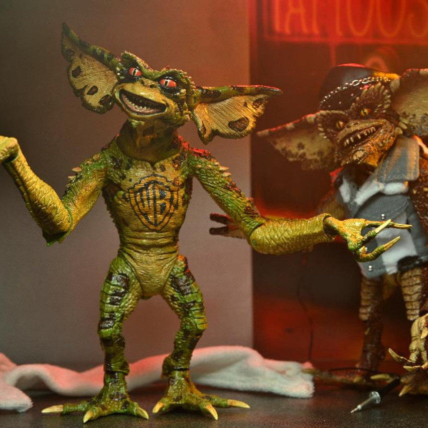 Two Gremlin action figures from the movie 'Gremlins' against a dark background with a neon sign.
